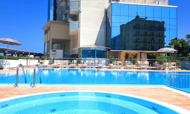 Piscina all'aperto di fronte a un hotel con riflessi sul vetro.