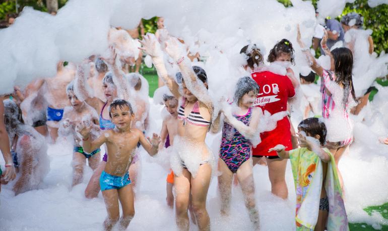 Bambini che giocano con la schiuma in una festa all'aperto.