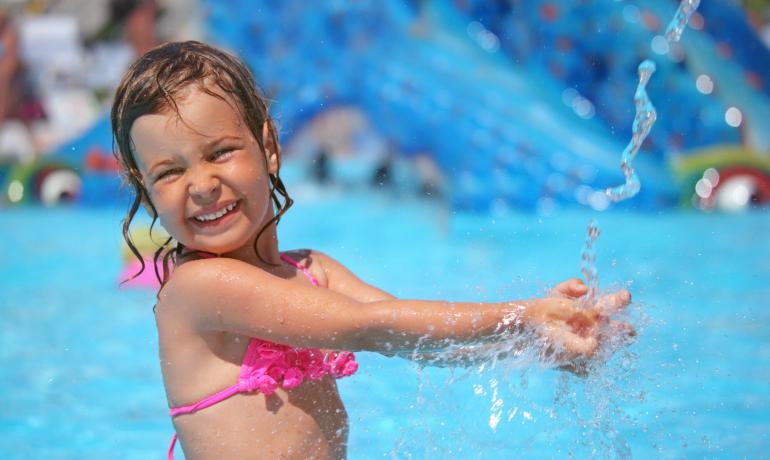 Bambina che gioca in piscina, sorridendo e spruzzando acqua.