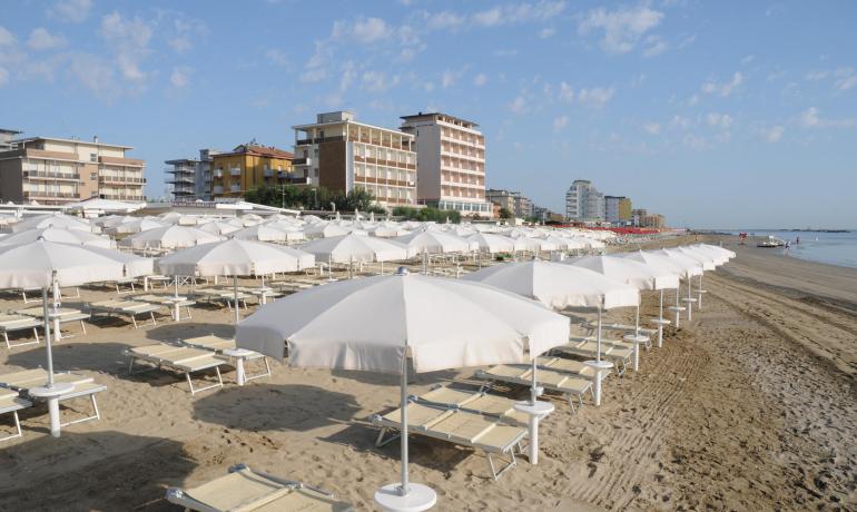 Spiaggia con ombrelloni bianchi e edifici sullo sfondo.