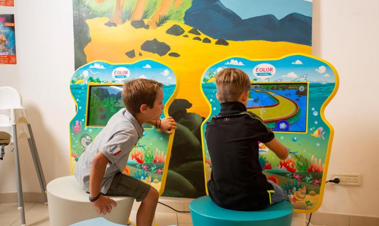 Bambini giocano a un videogioco interattivo in una sala colorata.