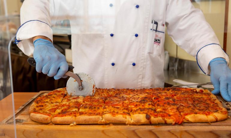 Chef taglia pizza rettangolare con rotella su tagliere di legno.