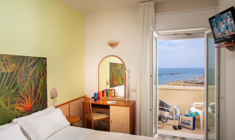 Camera con vista mare, balcone, TV e decorazioni tropicali.