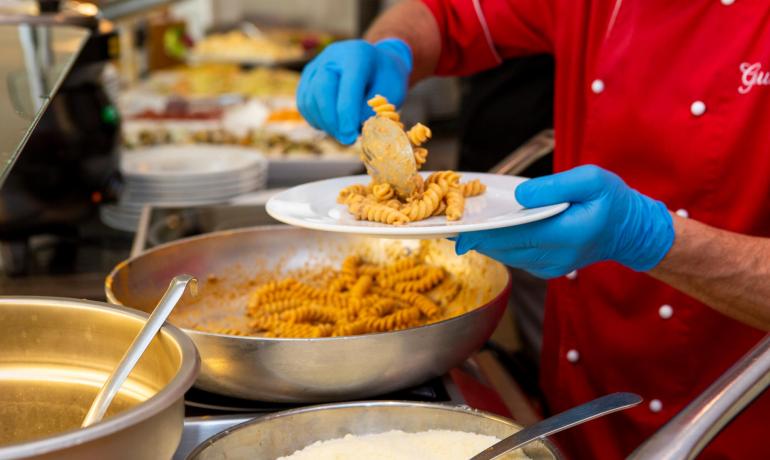 Chef serve pasta con guanti blu in un ristorante.