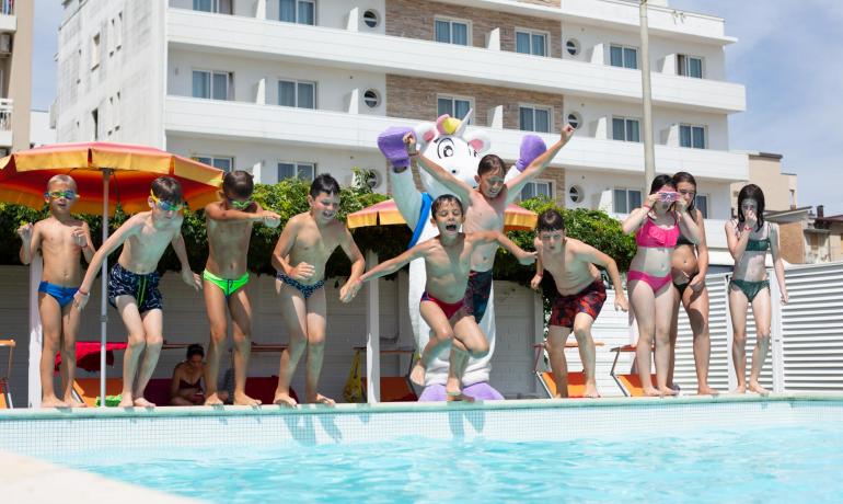 Bambini saltano in piscina con un costume da unicorno.