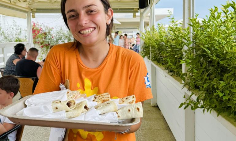 Ragazza sorridente con vassoio di cibo in un ristorante all'aperto.