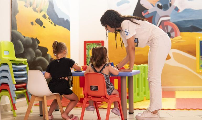 Insegnante aiuta bambini a colorare in aula colorata.