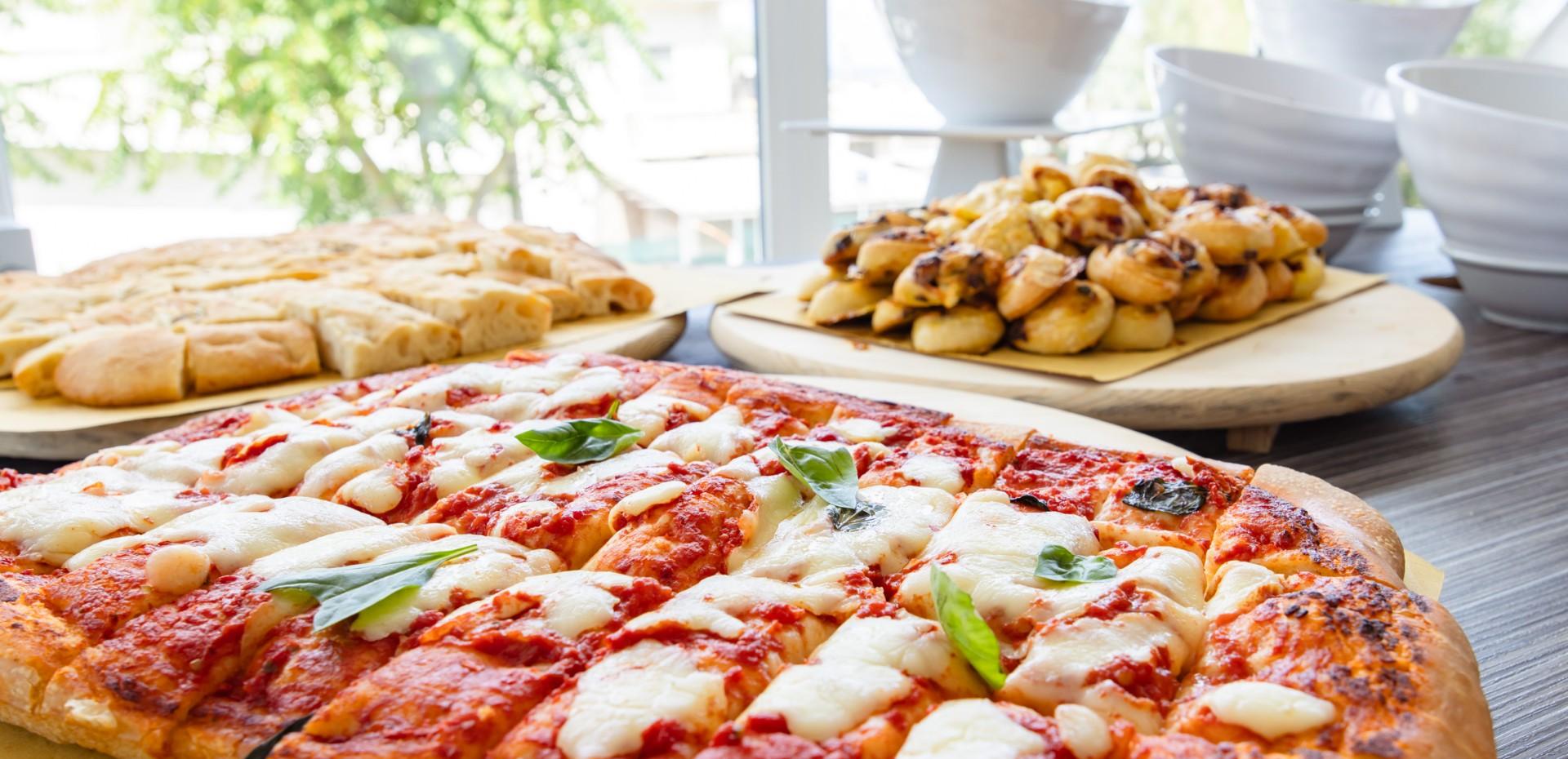 Pizza margherita con basilico e pane in secondo piano.