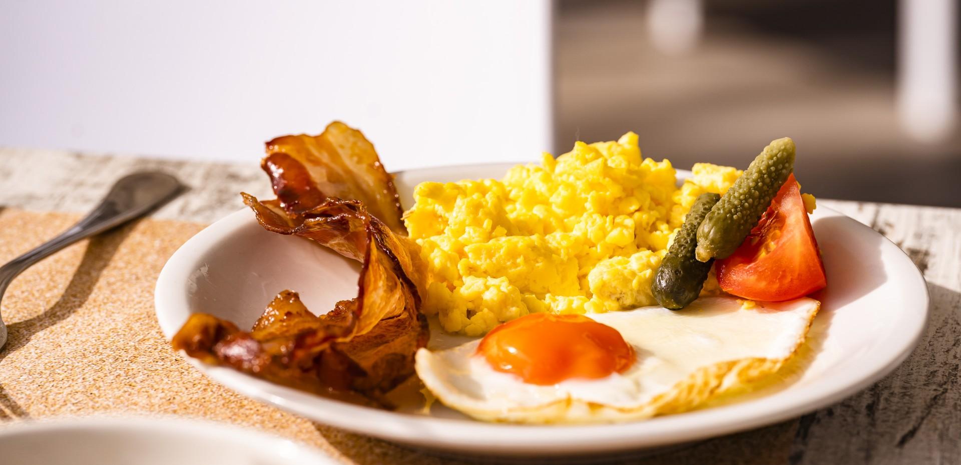 Colazione con uova, bacon, pomodoro e cetriolini.