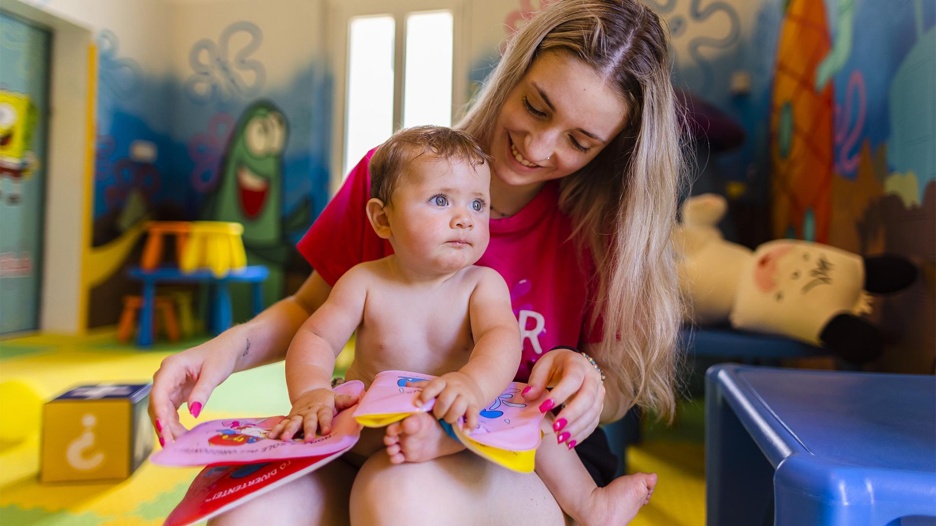 Bambino con braccioli arancioni vicino a piscina, ombrelloni colorati sullo sfondo.