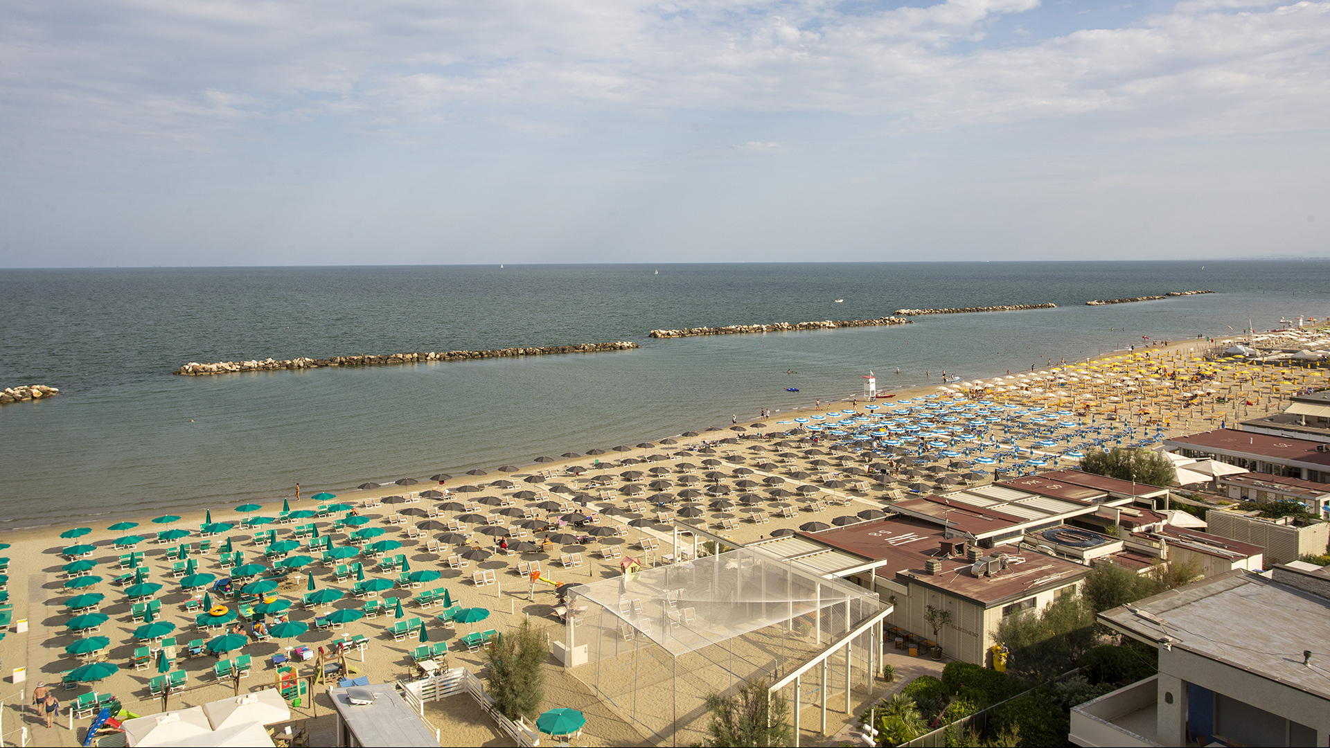 Famiglia cammina sulla spiaggia, tra ombrelloni e sdraio, verso il mare.