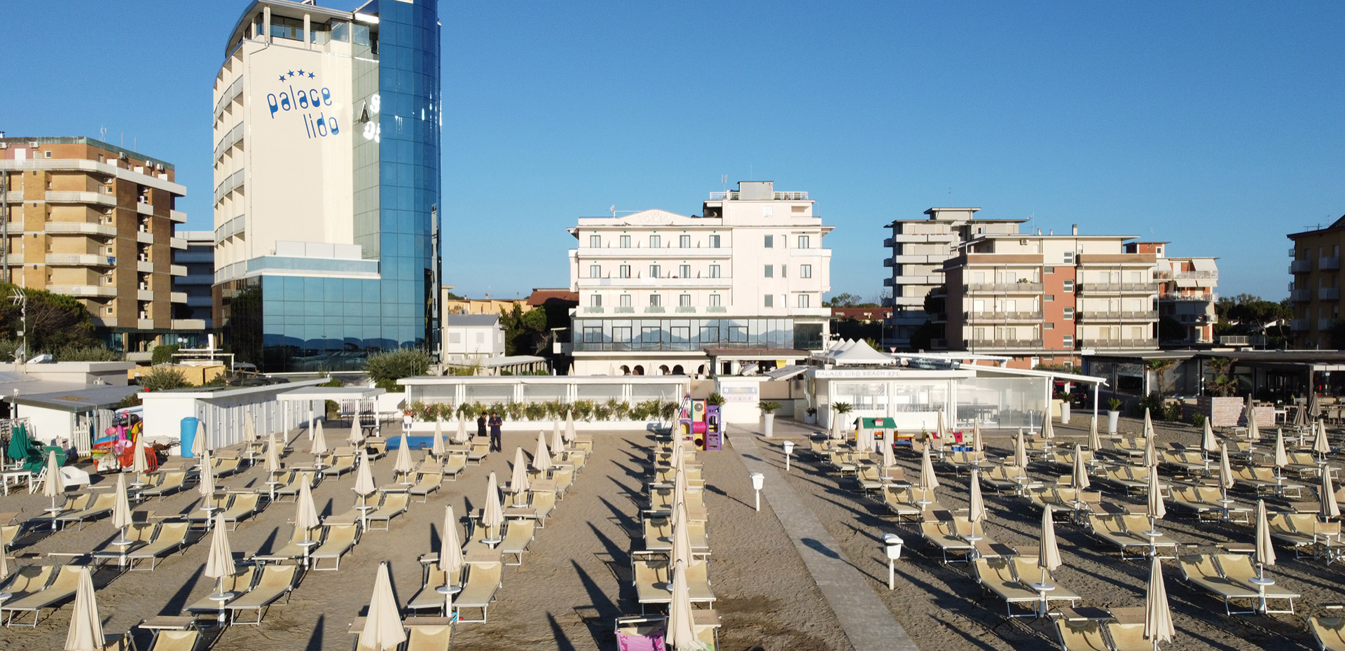 Papà e figlia sorridenti giocano sulla spiaggia con secchiello e paletta.