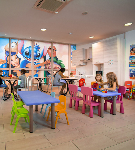 Area giochi per bambini con scivolo giallo e sedie colorate.