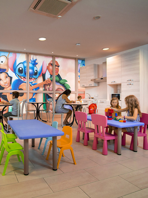 Area giochi per bambini con scivolo giallo e sedie colorate.
