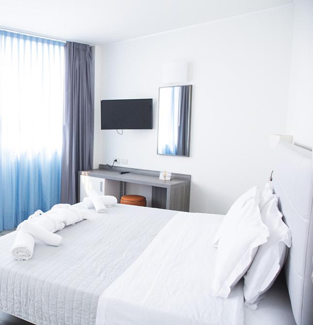 Camera luminosa e moderna, tende azzurre, letto ordinato, atmosfera rilassante.