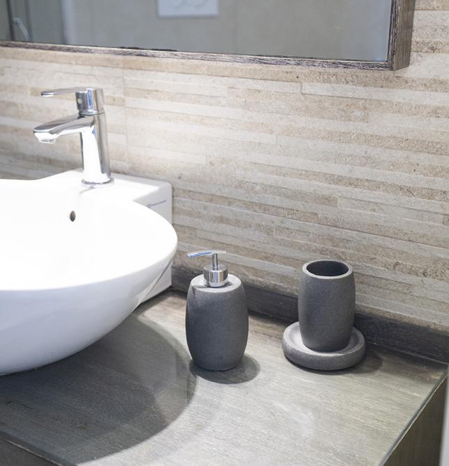 Elegante bagno moderno con lavabo bianco e accessori grigi su superficie in legno.