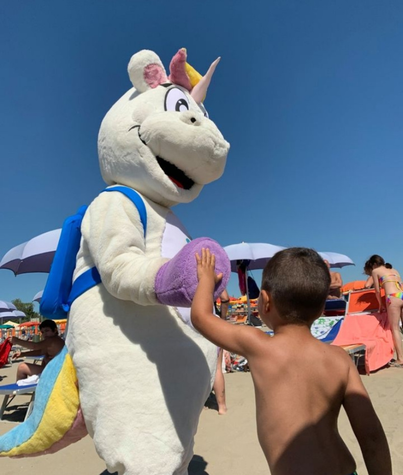 Bambino dà il cinque a un unicorno mascotte sulla spiaggia sotto il sole.