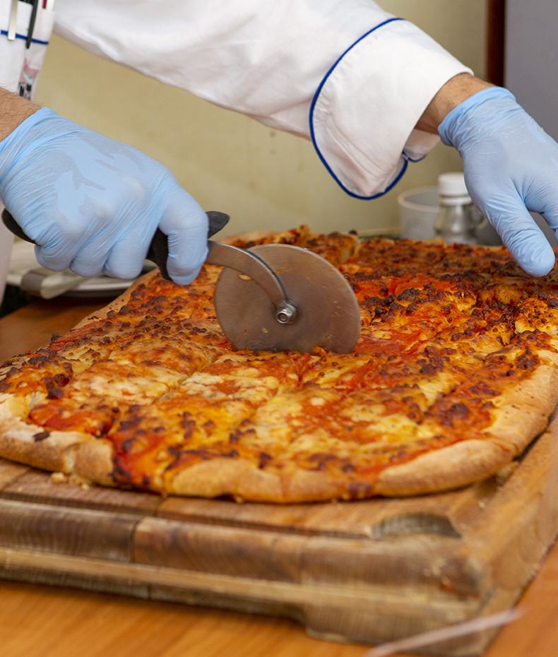 Chef slices a steaming pizza with a rolling cutter.