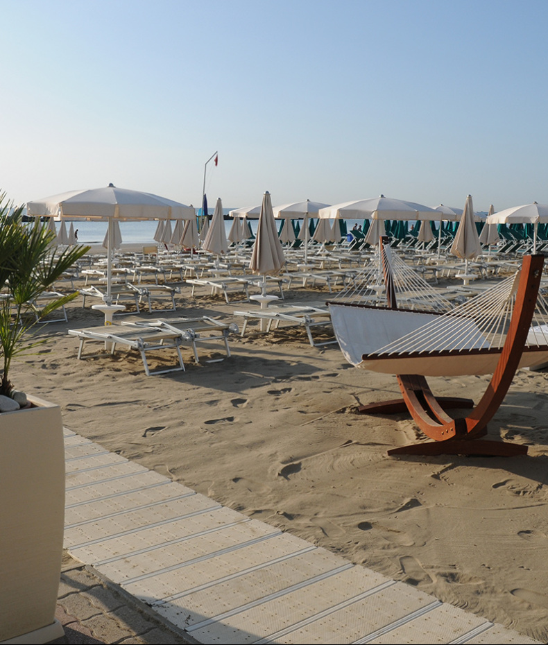 Ragazzo sistema ombrellone su spiaggia deserta, indossando occhiali da sole e maglietta blu.